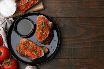 Tasty bread with tomatoes, parsley, salt and oil on wooden table, flat lay. Space for text
