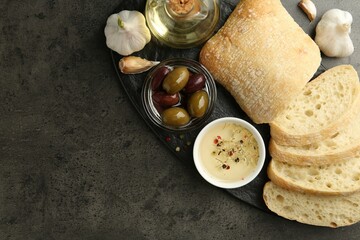 Sliced bread with oil, olives and spices on black table, flat lay. Space for text