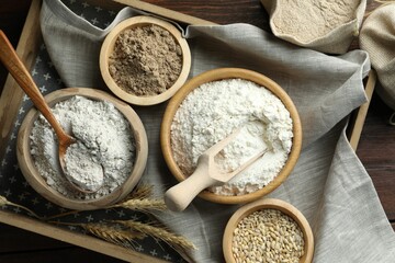 Different types of flour in bowls on wooden table, flat lay