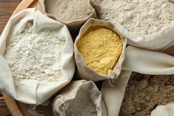 Different types of flour in bags on wooden table, flat lay