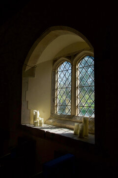  A  church window with three white candles on each side of the window on the window ledge, above and below the window the wall is black, ideal for copy space, Parish church, East Sussex, UK