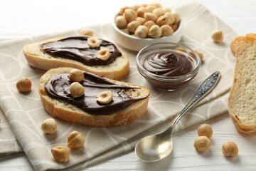 Slices of bread with chocolate spread and hazelnuts on white wooden table, closeup