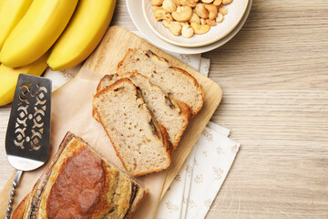 Cut banana bread with nuts, fruits and server on wooden table, flat lay. Space for text