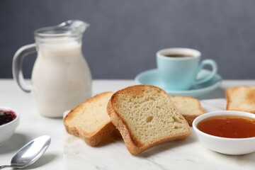 Slices of tasty toasted bread, milk and jam on white table against grey background, closeup