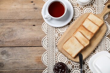 Slices of tasty toasted bread, jam and cup of tea on wooden table, flat lay. Space for text