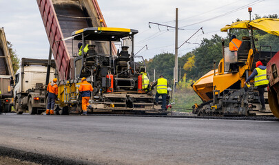 Two Asphalt Paver Machine laying fresh asphalt on road construction site.