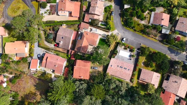 Drone captures peaceful residential area in Lacanau, France, featuring terracotta rooftops, pine trees, and tranquil green surroundings.