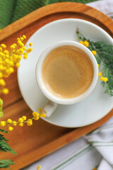 A warm spring morning setting with a cup of coffee placed on a wooden tray, surrounded by fresh mimosa flowers, perfect for a cozy breakfast.