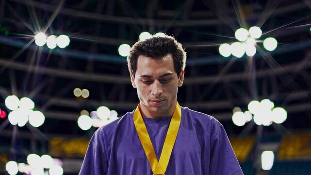Close up male athlete purple shirt medal looks downwards sombre expression bright stage lights background conveys disappointment defeat loss sadness after competition unfulfilled ambition grief