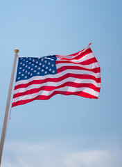 US flag proudly waving in the wind on a flagpole with golden sphere the finial ball on blue sky background. Copy space.