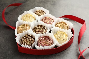 Flower shaped chocolate bonbons in box and red ribbon on grey table, closeup