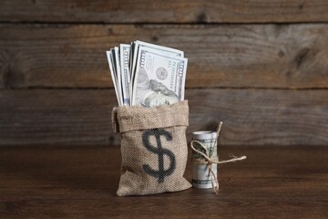 Burlap sack with dollar banknotes on wooden table