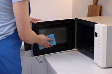 Woman cleaning microwave oven with rag indoors, closeup