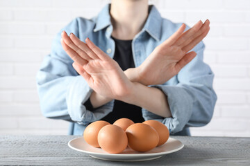 Woman refusing to eat eggs at grey wooden table, selective focus. Food allergy concept