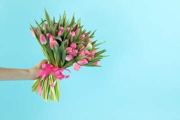 Woman with bouquet of beautiful tulips on light blue background, closeup. Space for text