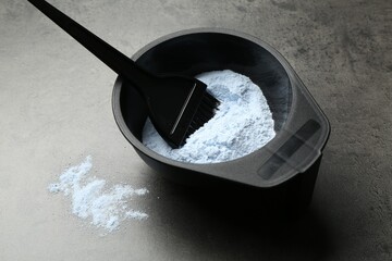 Bowl with hair bleaching powder and brush on grey table, closeup