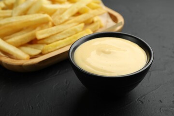 Tasty cheese sauce in bowl and French fries on black table, closeup