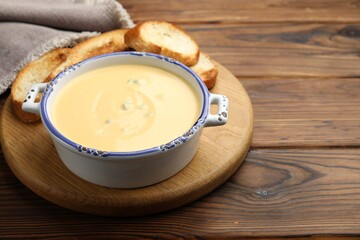 Tasty cheese dipping sauce in bowl and croutons on wooden table, closeup. Space for text