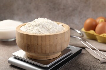 Digital kitchen scale with bowl of flour on grey textured table, closeup