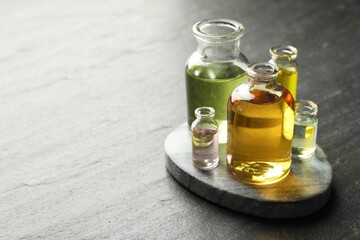 Open perfume bottles with aromatic essential oils on dark textured table, closeup. Space for text