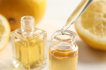 Dripping aromatic essential oil from pipette into perfume bottle at white table, closeup