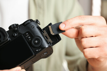 Man inserting SD memory card into photo camera indoors, closeup