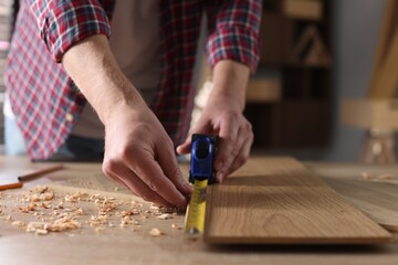 Man measuring wooden plank with tape indoors, closeup