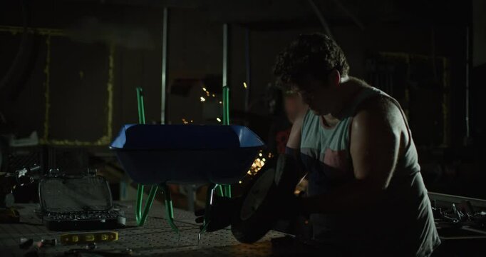 Silhouette of man attaching wheel to wheel-barrow in busy shop - dolly in slow motion