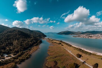 Obraz premium Aerial view showcases a river flowing into the ocean surrounded by mountains and blue sky.