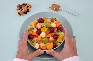 Female hands holding a green bowl full of fresh and colorful fruit. Apple, kiwi, orange, papaya, grape, mango, melon. Breakfast or break, healthy eating
