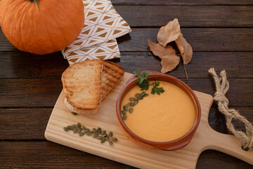 A pumpkin creamy soup in a bowl served with pumpkin seeds and croutons. Vegan soup. Dark wooden...