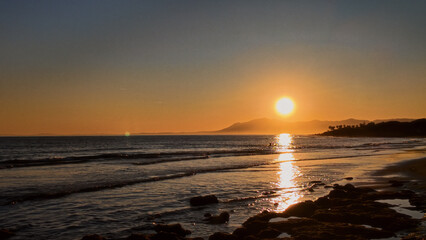 Golden sunset reflecting on the rippling water of Marbella beach in Spain