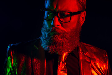 Charismatic mature man in glossy suit with a groomed beard and glasses against a dark neon...