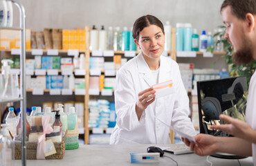 Obraz premium Female pharmacist offers to buy pills for man at a pharmacy