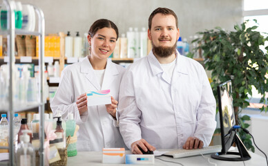 Obraz premium Pharmacists stand near the counter and present new arrivals in the pharmacy. Two pharmacists stand near a computer and invite to shop in a European pharmacy