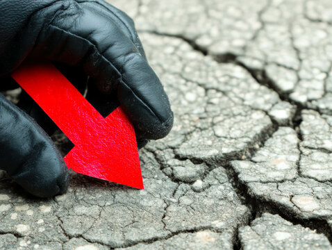 Gloved hand holds red arrow pointing down against cracked concrete symbolizing market collapse