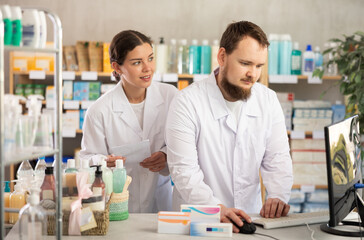 Obraz premium Qualified male and female pharmacists work at a computer, renew stocks in the warehouse, enter new arrivals of medicines and pills. Pharmacists working behind the counter in a pharmacy
