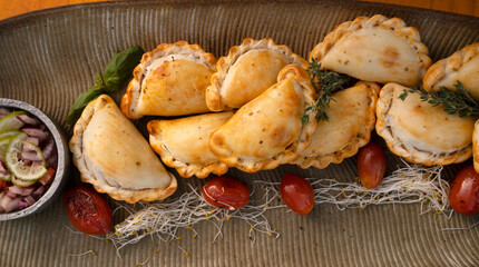 Hot finger food with a rustic presentation. Top view of gourmet traditional crispy meat empanadas with criolla sauce on the wooden table