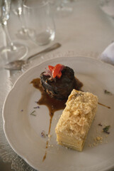 Gourmet gastronomy in a social event. Closeup view of a  grilled loin fillet with sauce and a potato mille feuille in a white dish on the gala table 