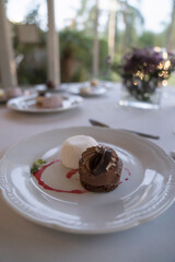 Gourmet menu in a social event. Desserts. Closeup view of a chocolate marquise with ice cream in a white dish. Beautiful silverware and table arrangement