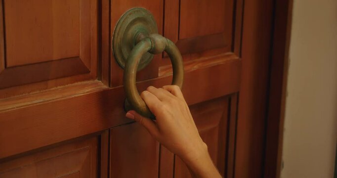 Closeup of woman hand knocking on wooden door with vintage ring knocker in Italy