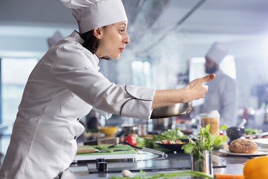 Skilled chef working over a stovetop cooking vegetables in oil with kitchen tools and utensils. Woman expert at the kitchen counter preparing fresh produce, emphasizing the artistry of food prep.