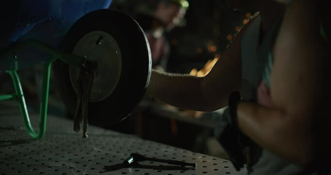 Guy in metal shop working on wheel barrow with sparks in the background - dolly in shot