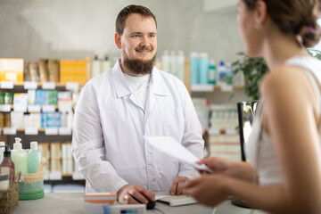 Obraz premium Young man pharmacist looking for prescription on computer to young woman buyer in pharmacy