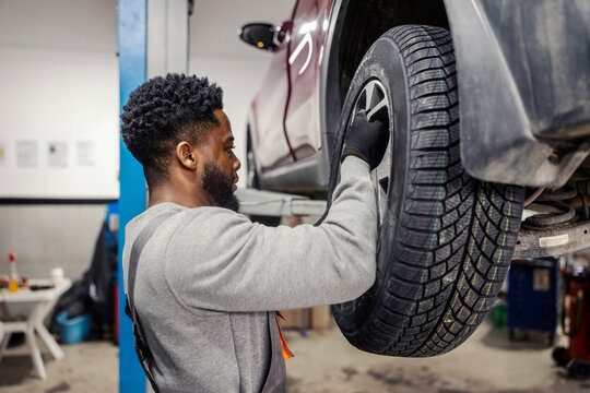 Side view of interracial handyman fixing car and changing tire at auto mechanic workshop.