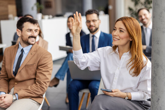 A businesswoman sitting at training room with hand raised and asking questions.