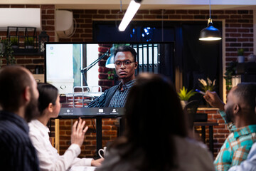 Professional black man seen on digital monitor during video call with colleagues. Male entrepreneur collaborates remotely with diverse team, discussing marketing strategy and project deadlines.