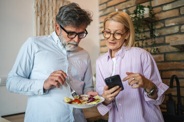 mature woman show mobile phone screen to man eating salad