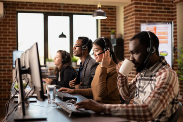 Diverse telemarketers seated at their workstations, communicating with remote clients and handling business requests. Coffee, headsets, and computers emphasizing customer support office environment.