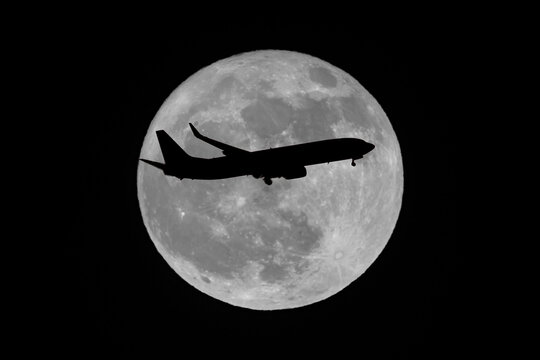 Silhouette of airliner flying in front of moon